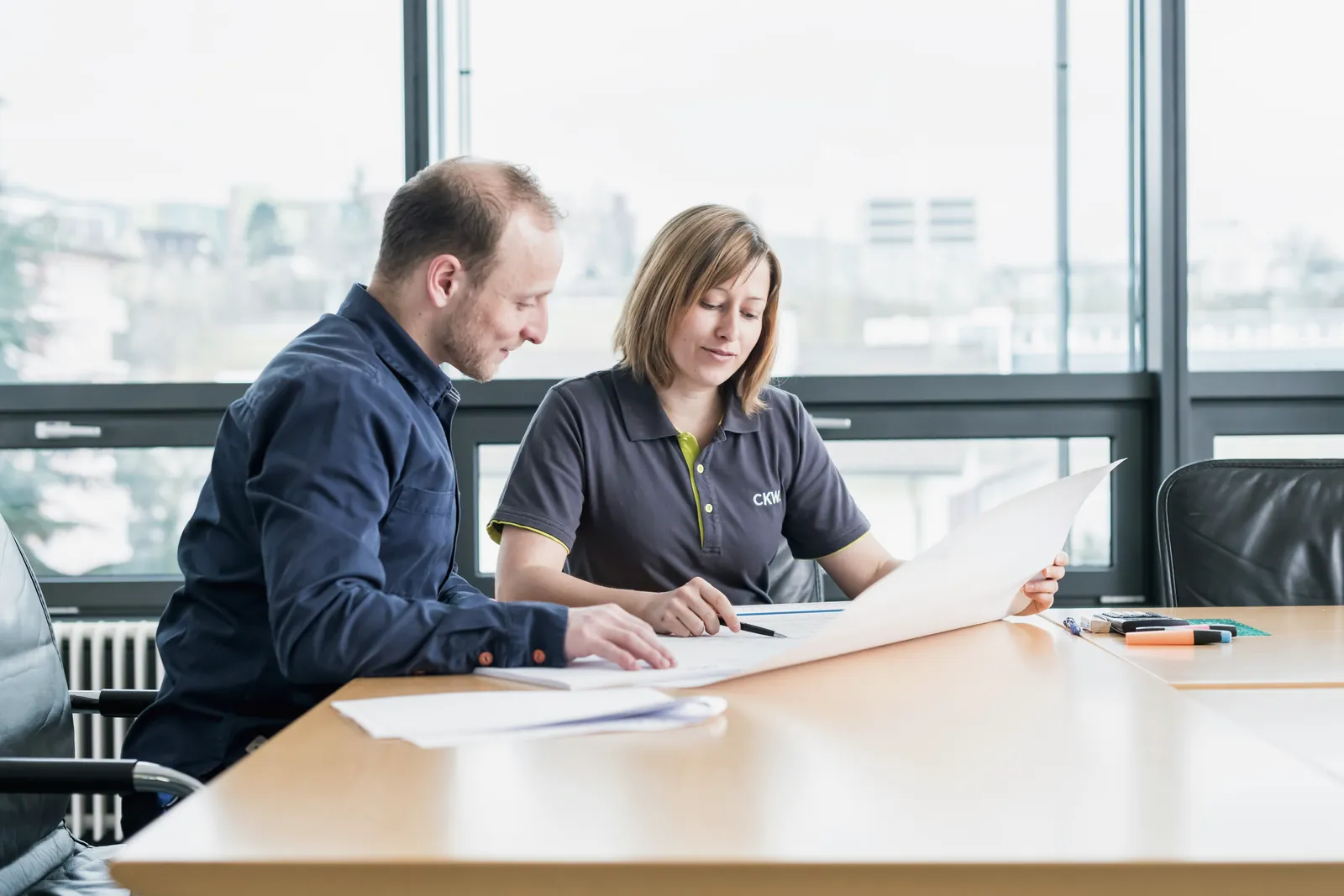 Two colleagues reviewing a printed document together, heads down.