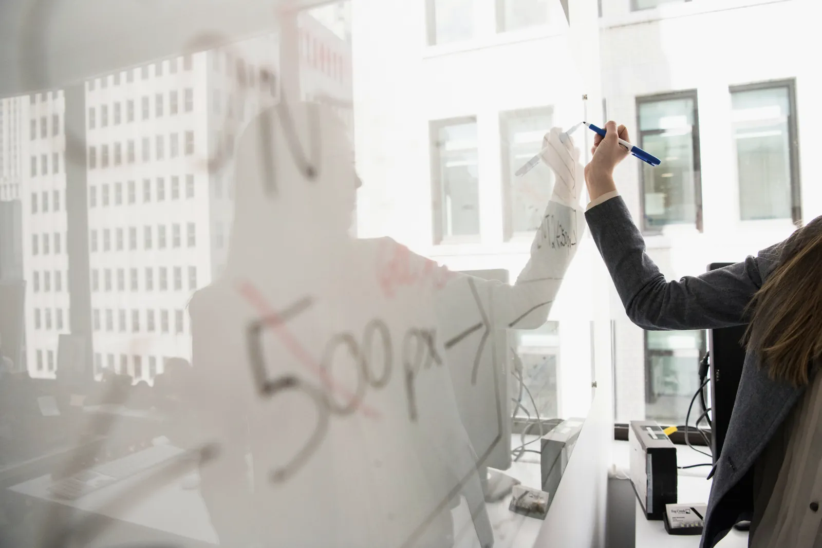 A hand writing on a glass whiteboard, no faces visible.